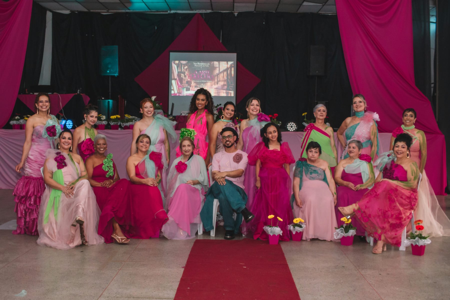 Participantes do desfile, em vestidos rosa e verde, reunidas com o estilista William Malagres diante do palco