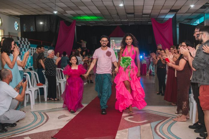 William Malagres caminha na passarela de mãos dadas com uma menina e uma modelo, aplaudidos pelo público